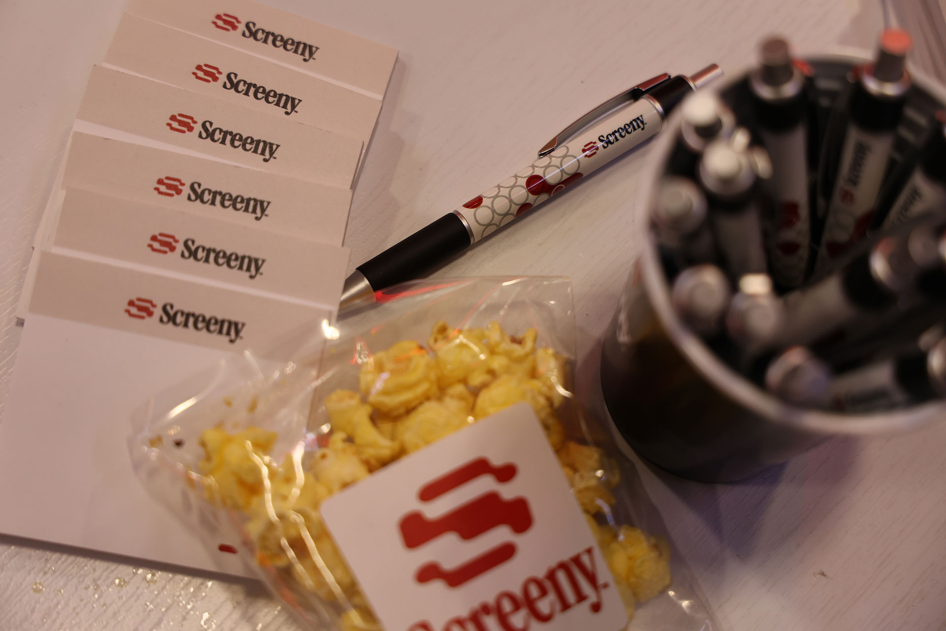 Screeny-branded cards, pens and a bag of Screeny popcorn on a table